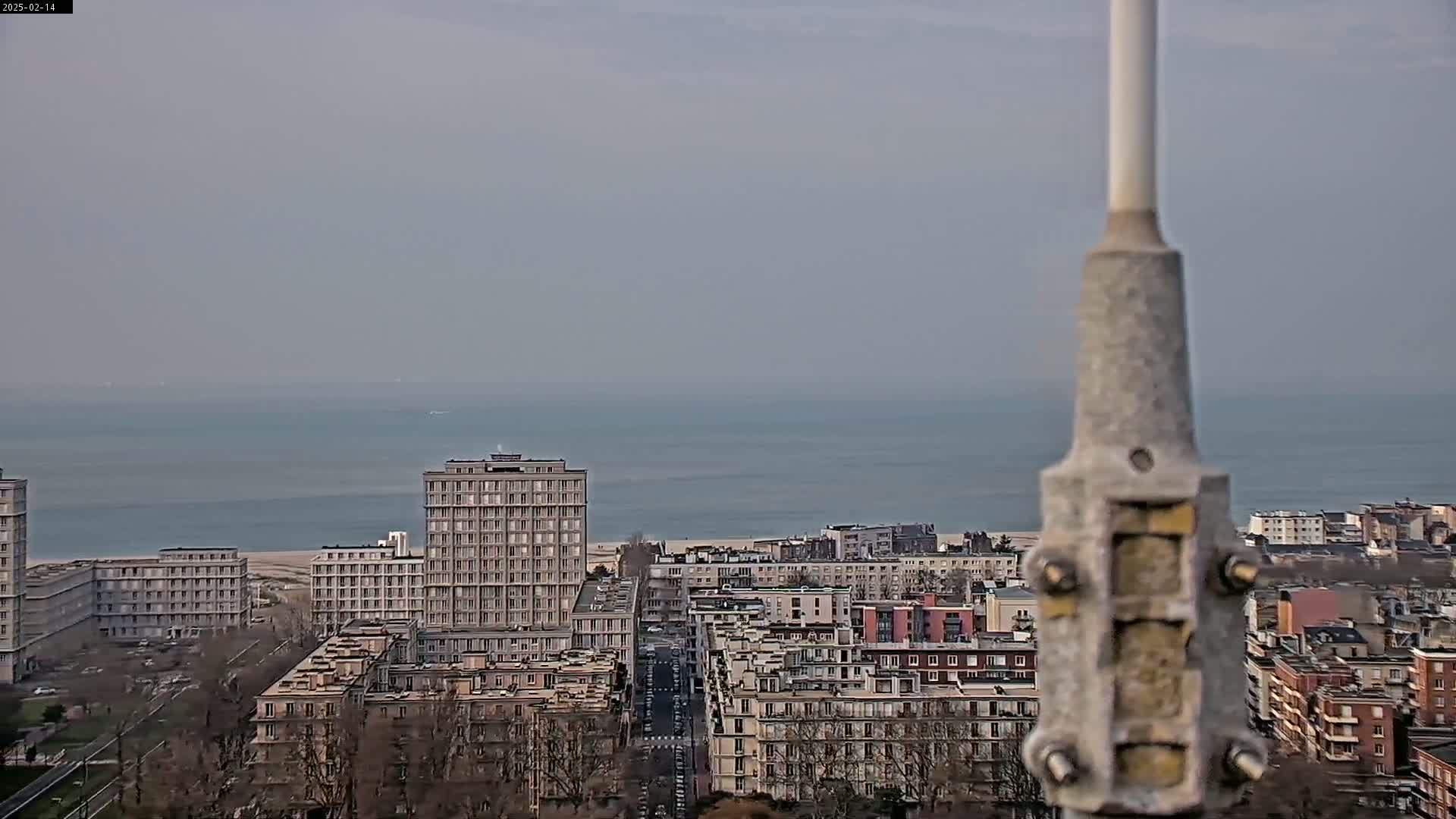 A cityscape with several multi-story buildings overlooks a calm ocean under an overcast sky.