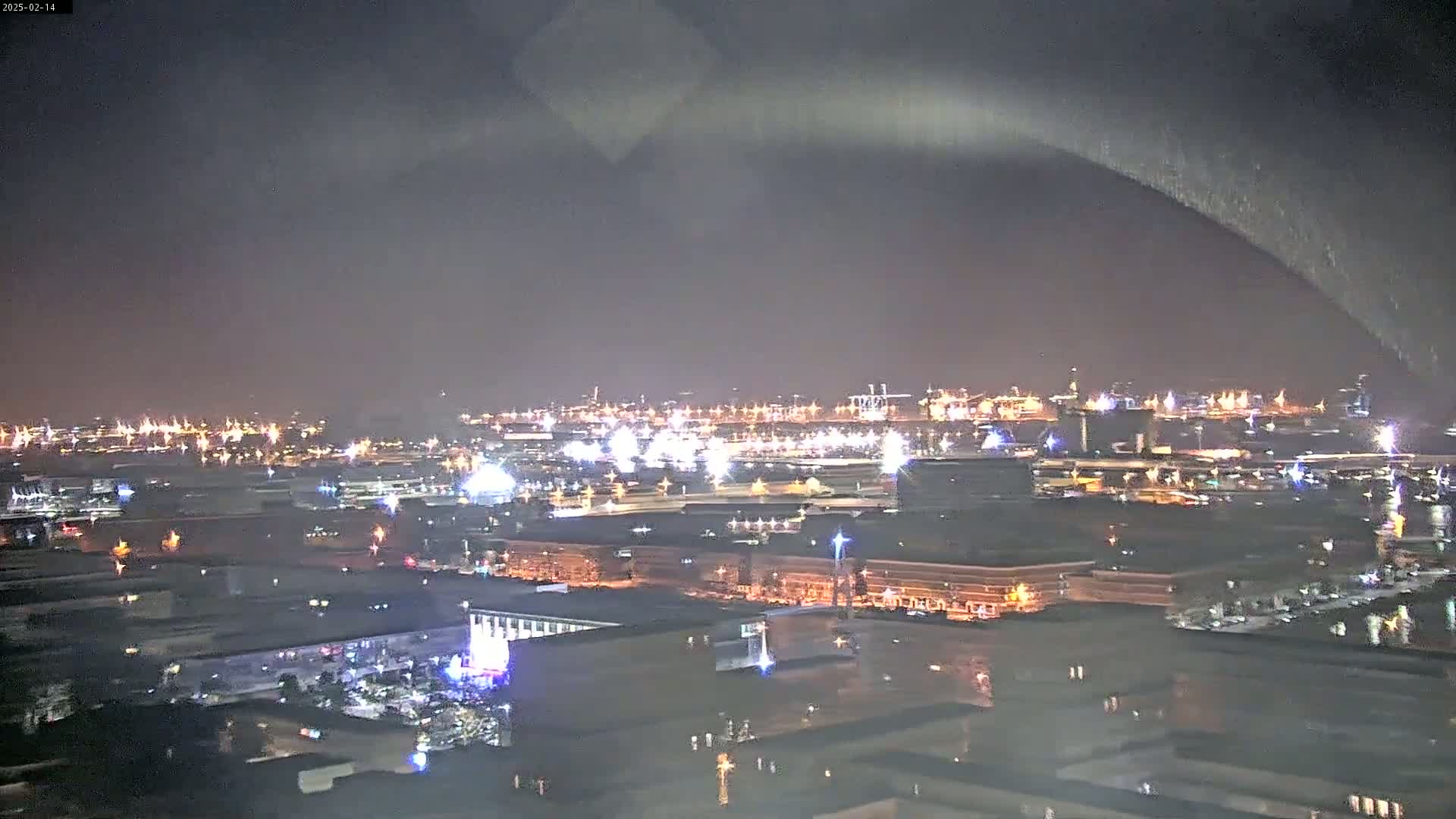A nighttime, aerial view of a city and port illuminated by numerous lights under an overcast sky.