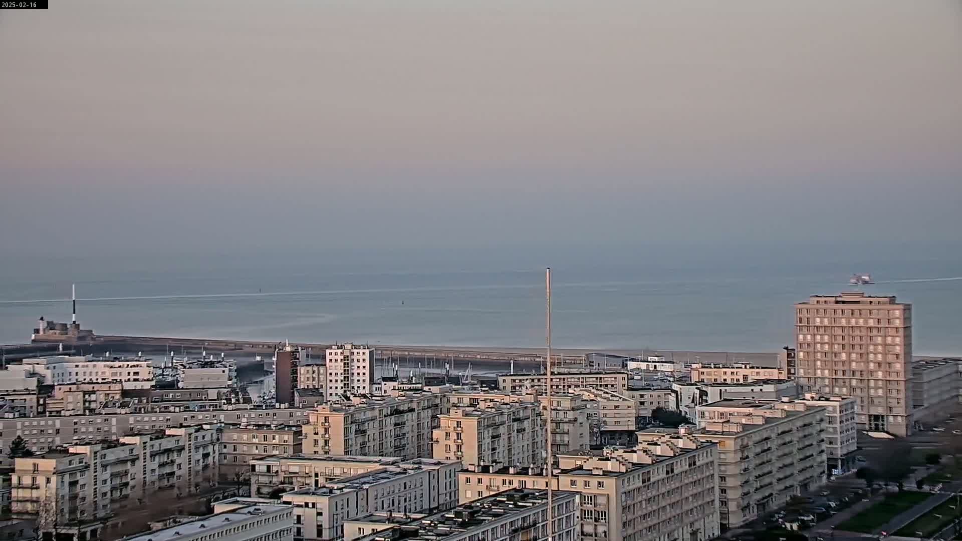 A coastal city with numerous apartment buildings is visible, overlooking a calm sea under a hazy sky.