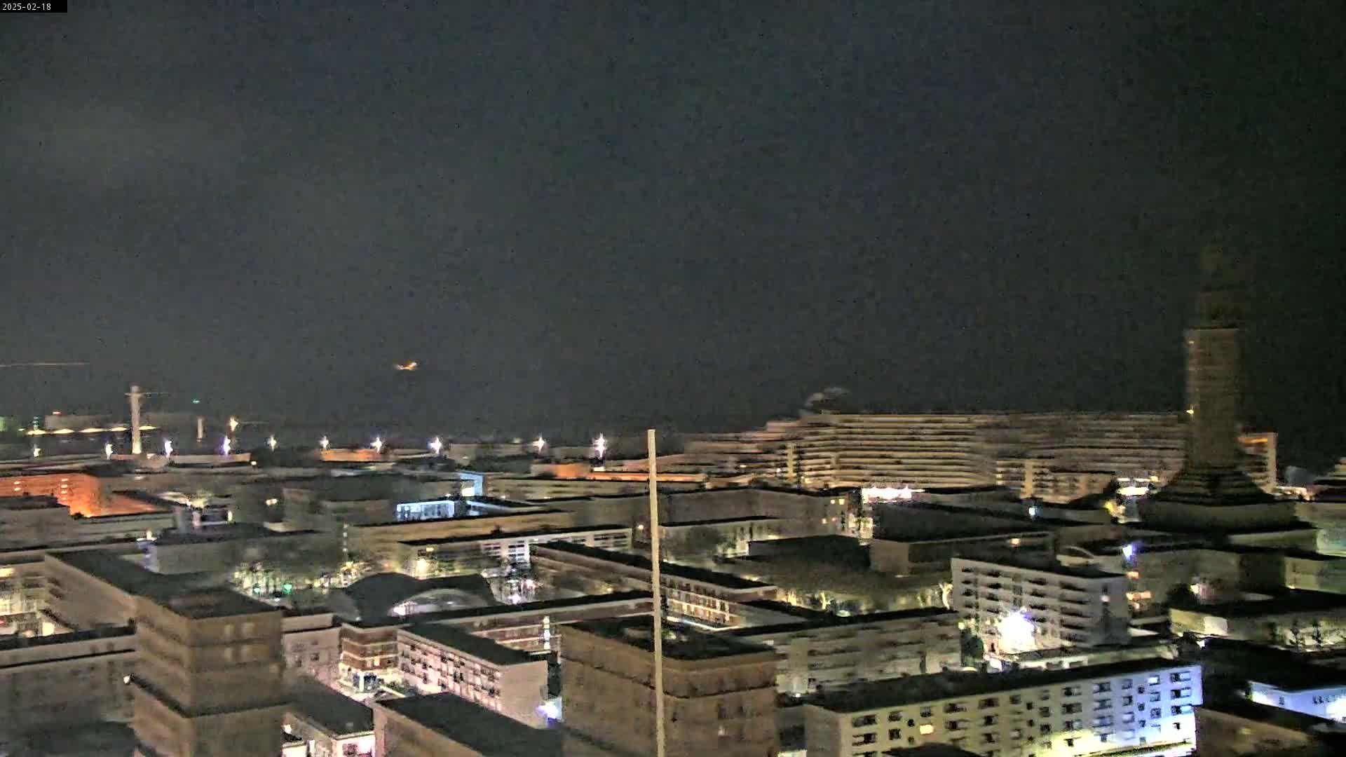 A nighttime aerial view of a city with numerous buildings illuminated under a dark, overcast sky.