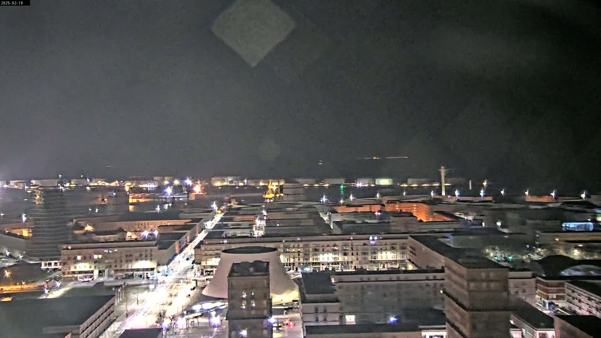 A nighttime, high-angle view of a city illuminated by streetlights and building lights, with a dark sky above.
