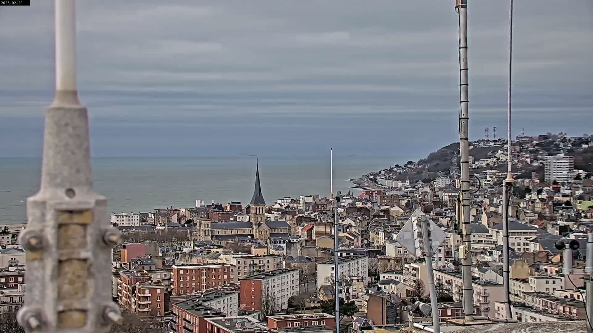A coastal city with a prominent church steeple is viewed from a high vantage point on an overcast day.