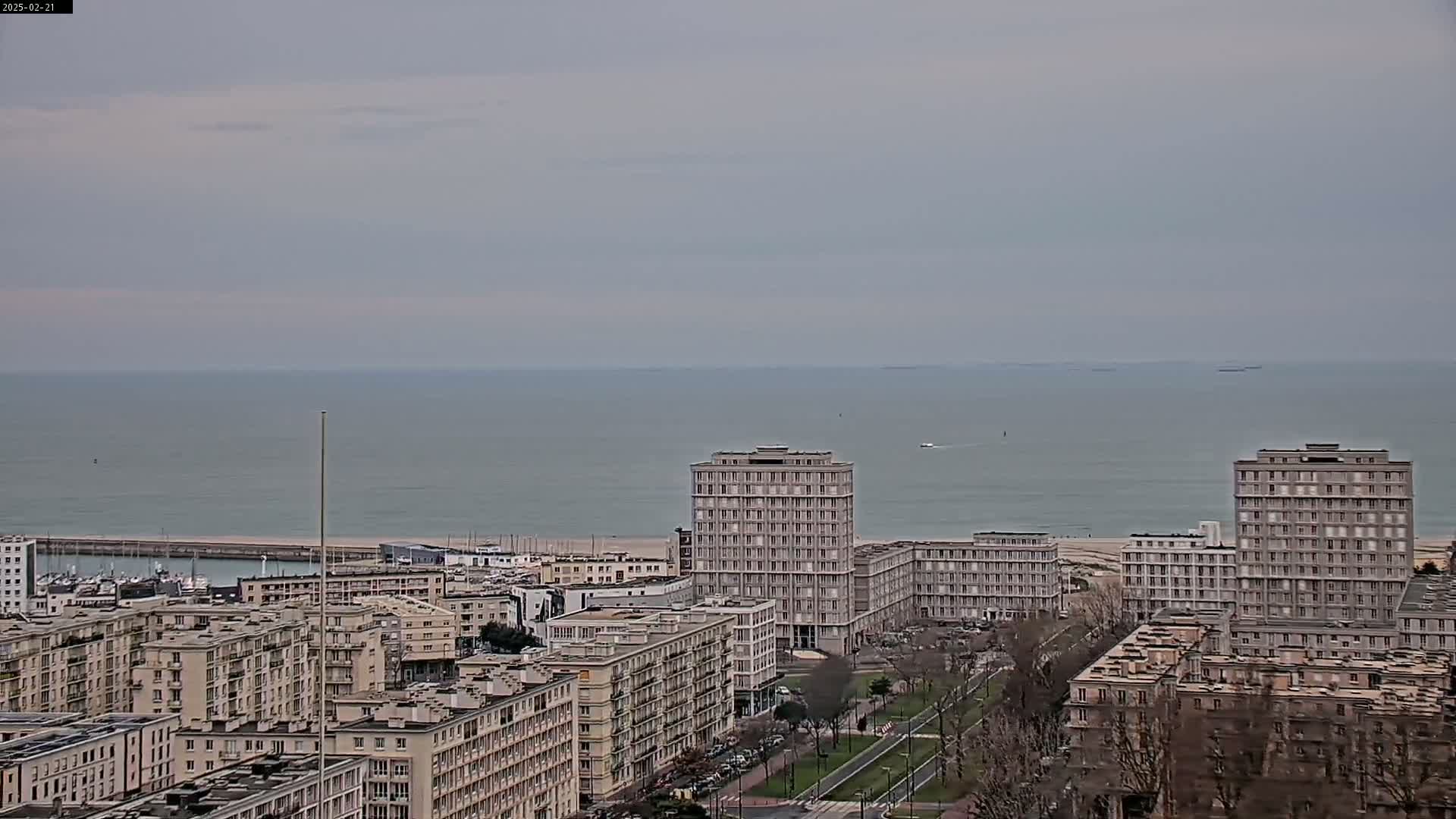 A coastal city with several high-rise buildings is seen on an overcast day with a calm sea in the background.