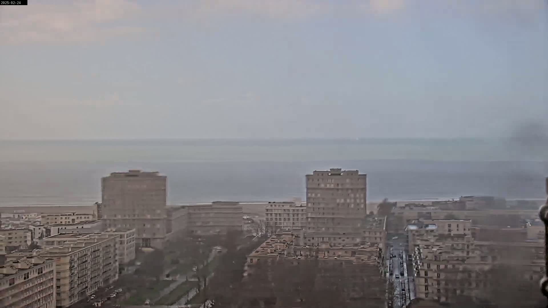 A hazy, overcast day reveals a coastal cityscape with several multi-story buildings and a distant ocean.
