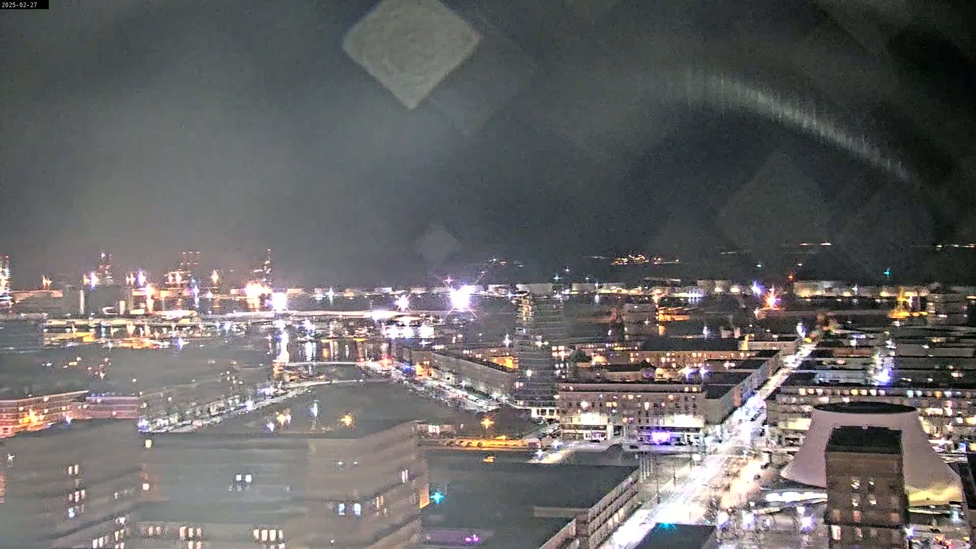 A nighttime aerial view of a city illuminated by streetlights and building lights, with a partly cloudy sky.