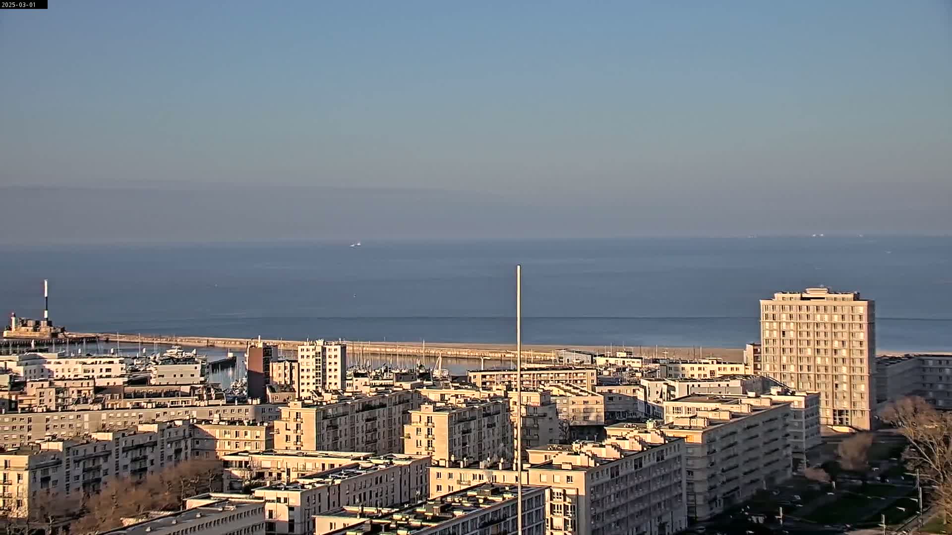 A coastal city with numerous apartment buildings is visible, overlooking a calm sea under a clear sky.