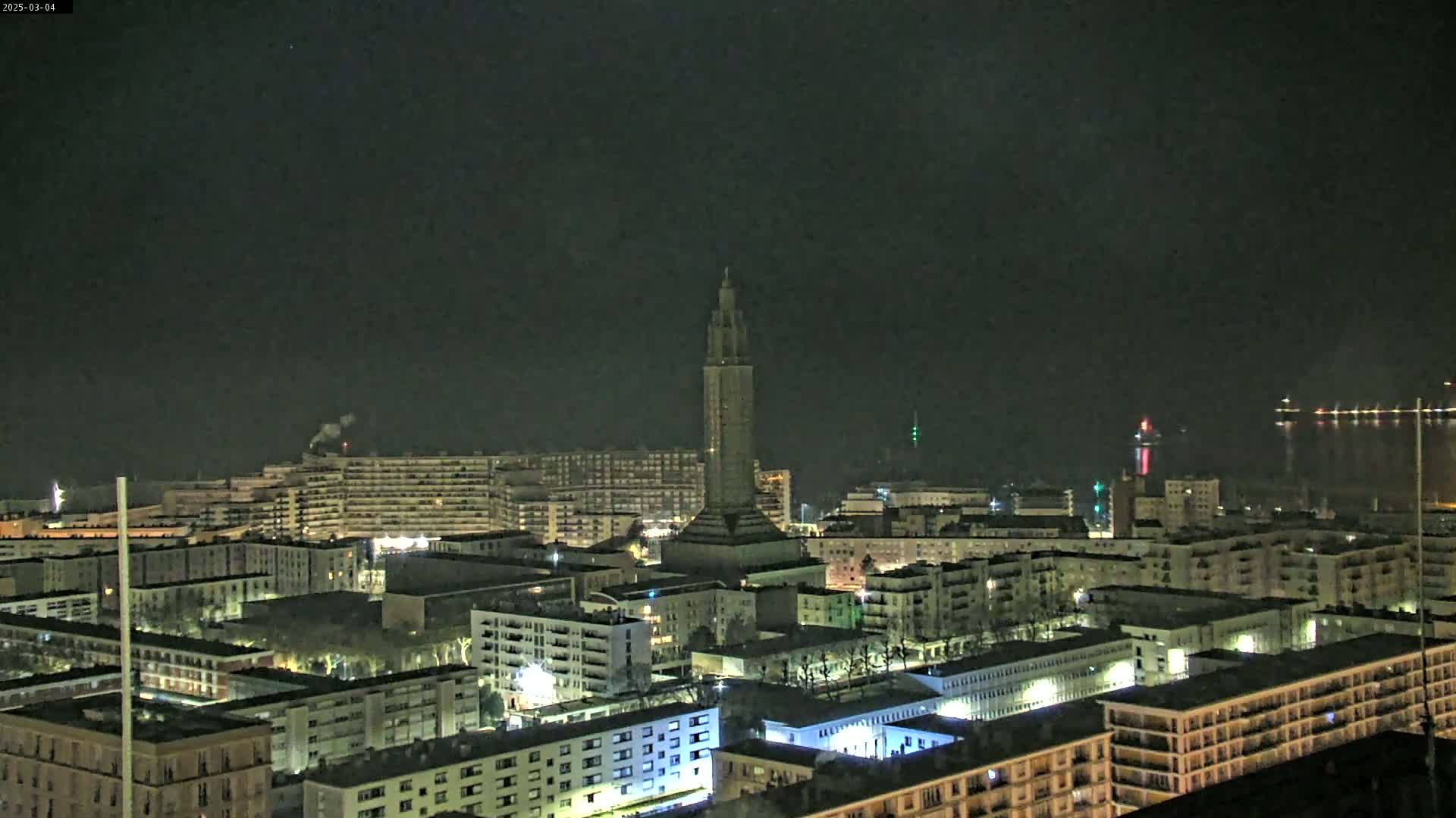 A nighttime aerial view of a city with a tall tower at its center, under a dark, clear sky.