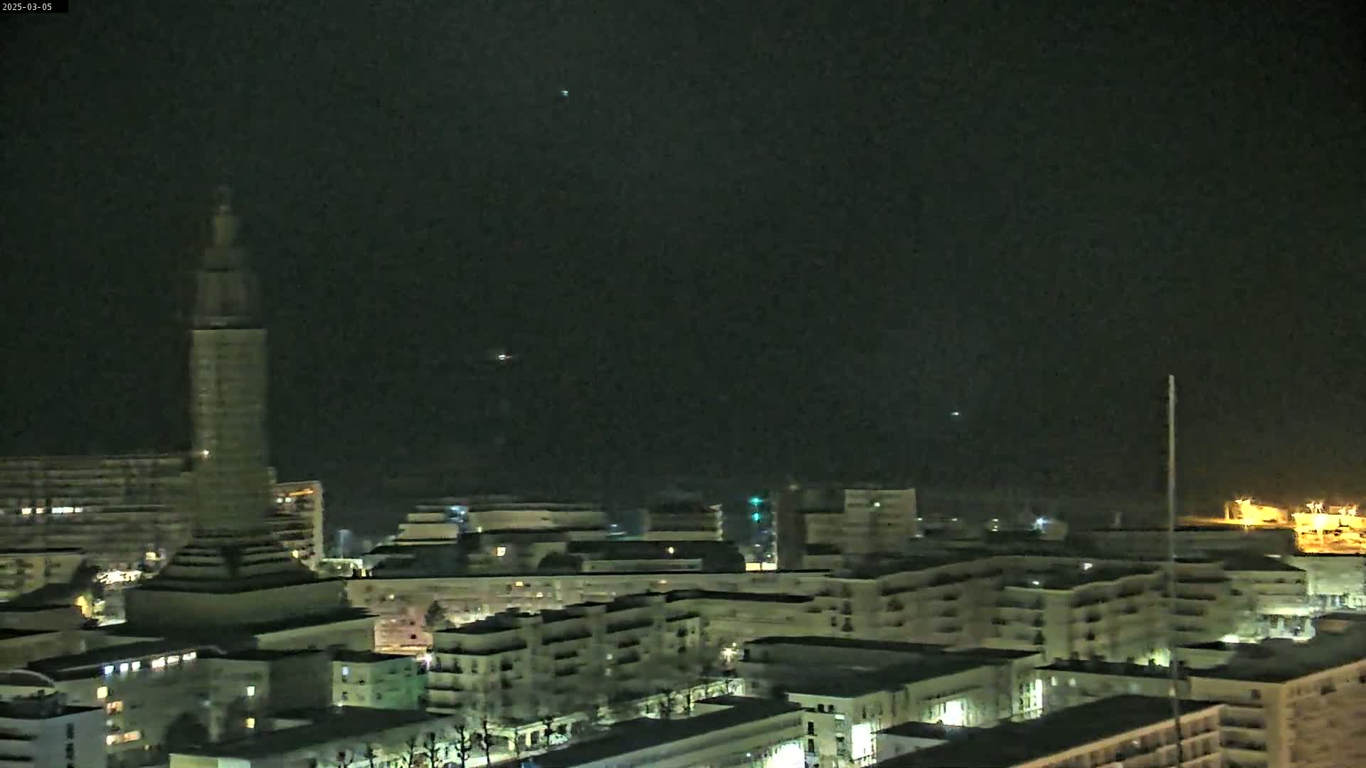 A nighttime view of a city skyline featuring a tall tower, numerous buildings, and a dark, clear sky.