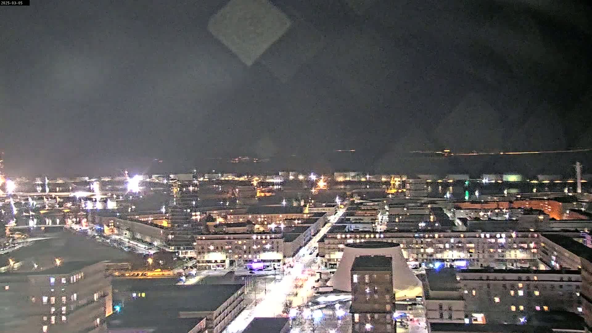 A nighttime aerial view of a city with a body of water in the background under a dark sky.