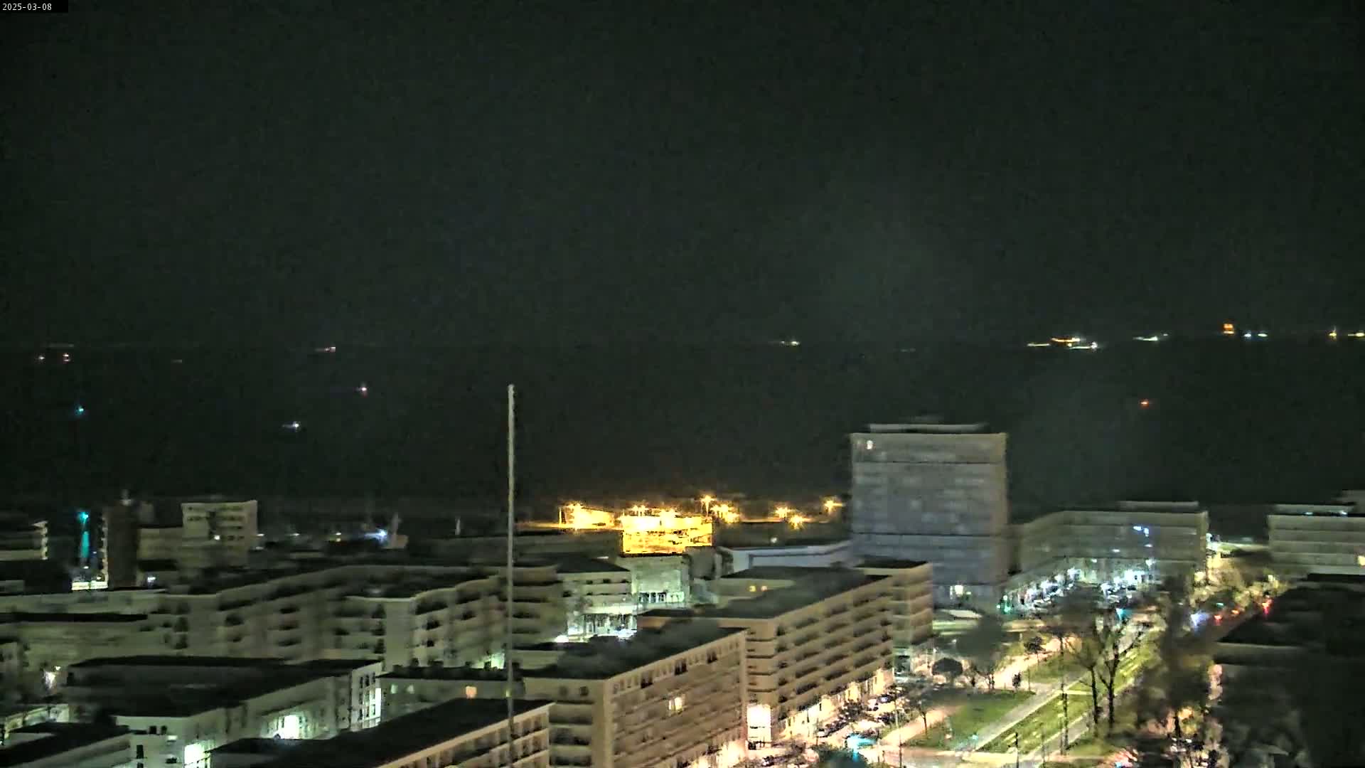 A nighttime view of a city illuminated with lights overlooking a dark body of water under a clear sky.