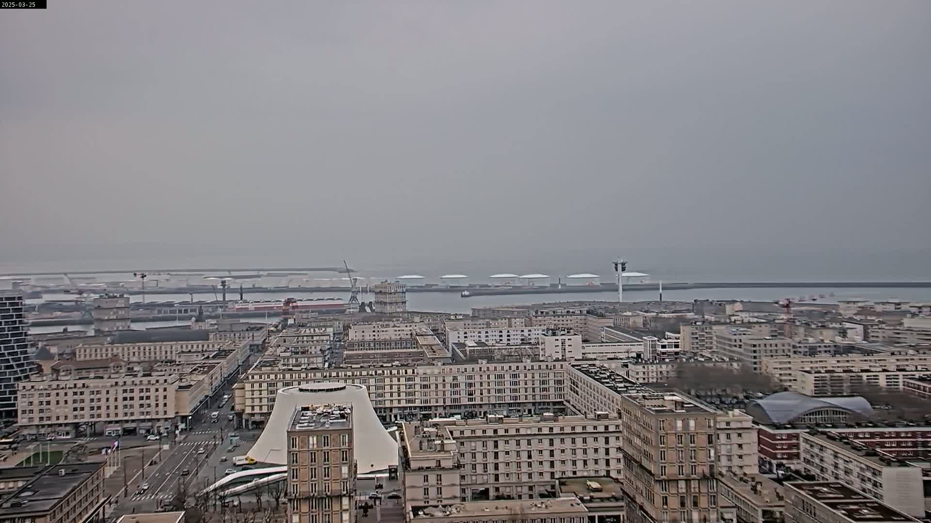 A hazy, overcast day reveals a sprawling cityscape overlooking a harbor with numerous vessels and industrial structures.