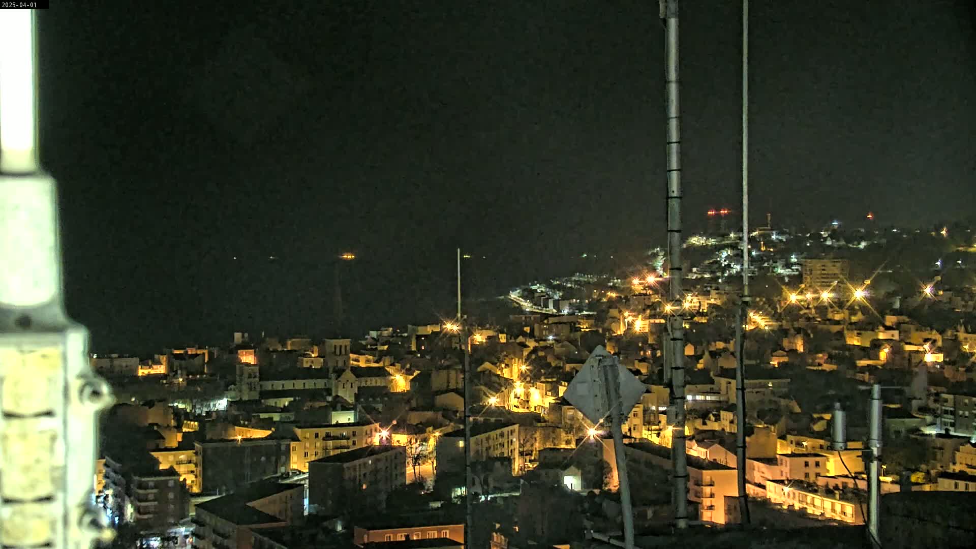 A nighttime view of a coastal town illuminated by streetlights, with a dark ocean visible in the distance.