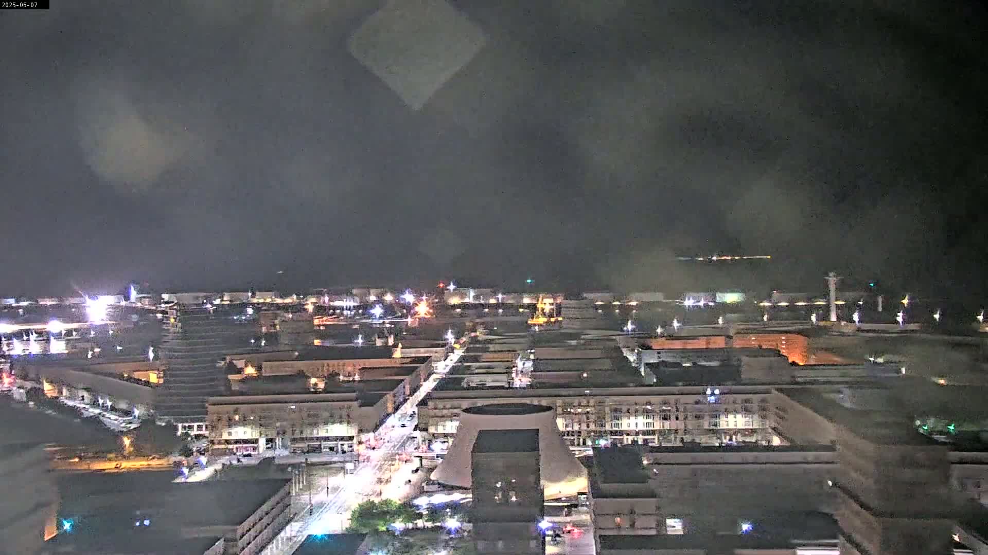 A nighttime, hazy view of a city illuminated with streetlights, featuring a large, dome-shaped building near the center.