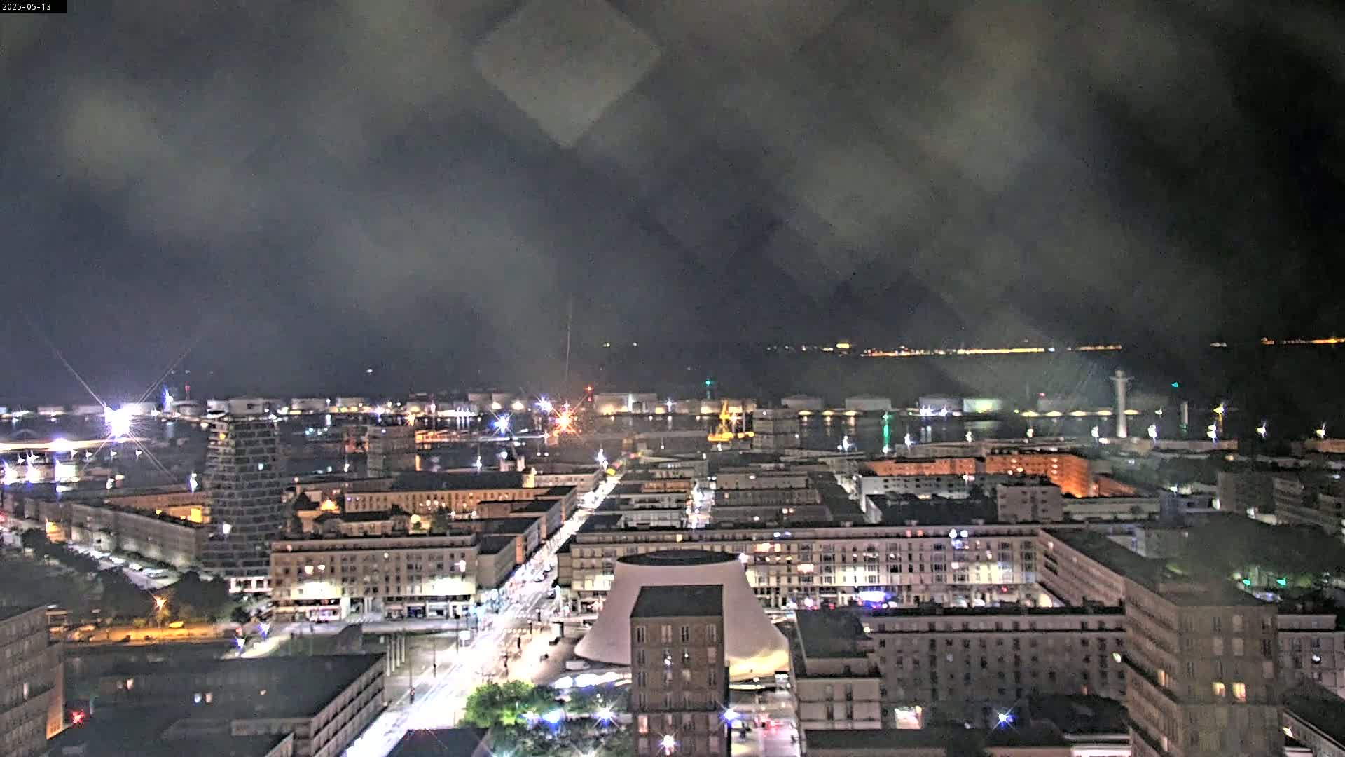 A nighttime, hazy view of a city's harbor and buildings, with a body of water visible in the distance.