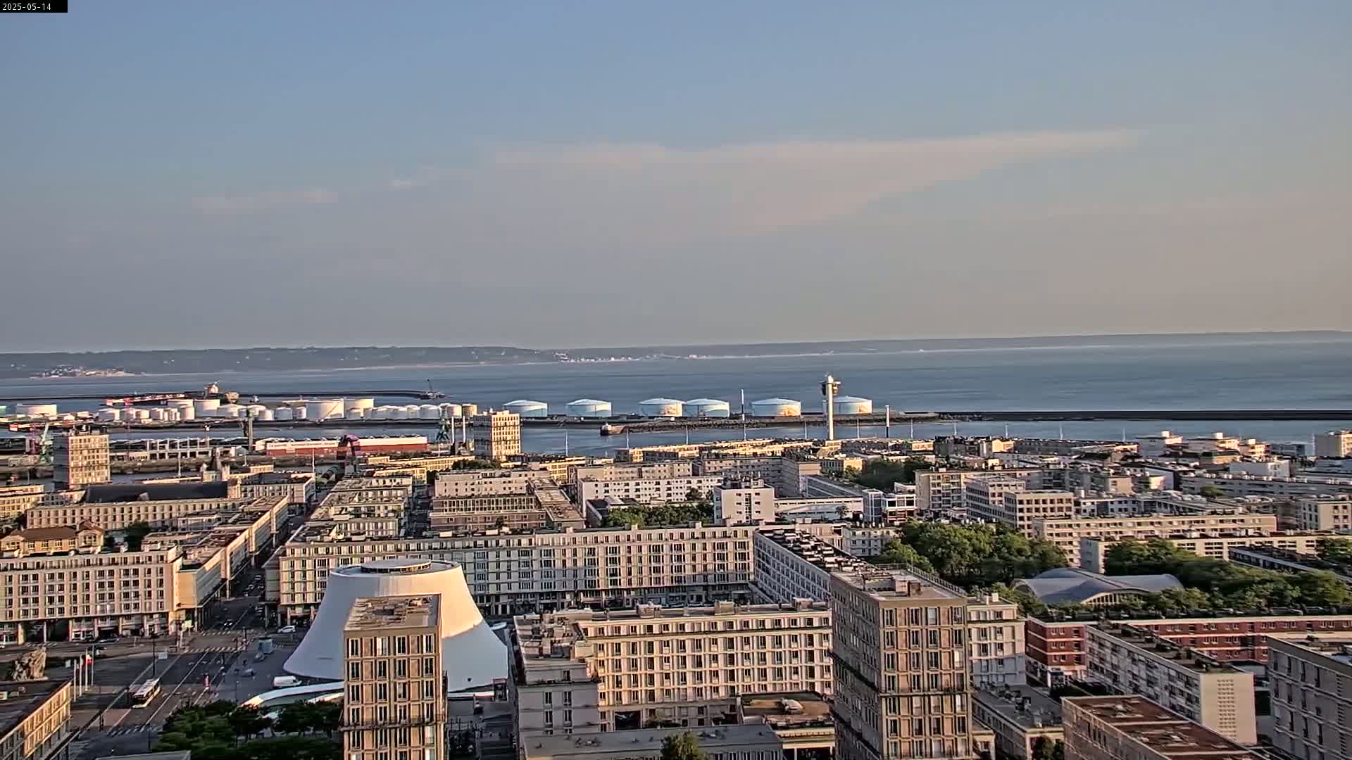A coastal city with numerous buildings, a large body of water in the background, and a clear sky.
