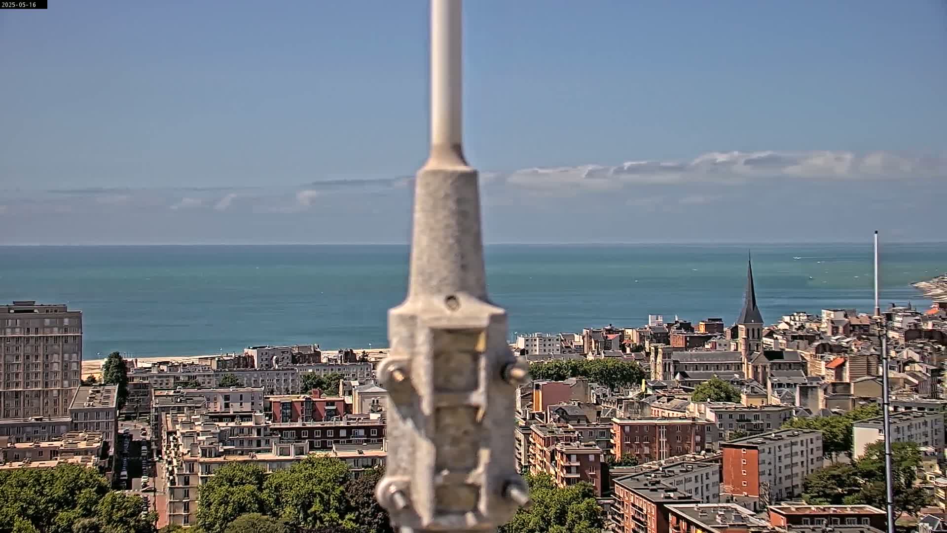 A coastal city with a beach and many buildings is visible beyond a tall pole on a partly cloudy day.