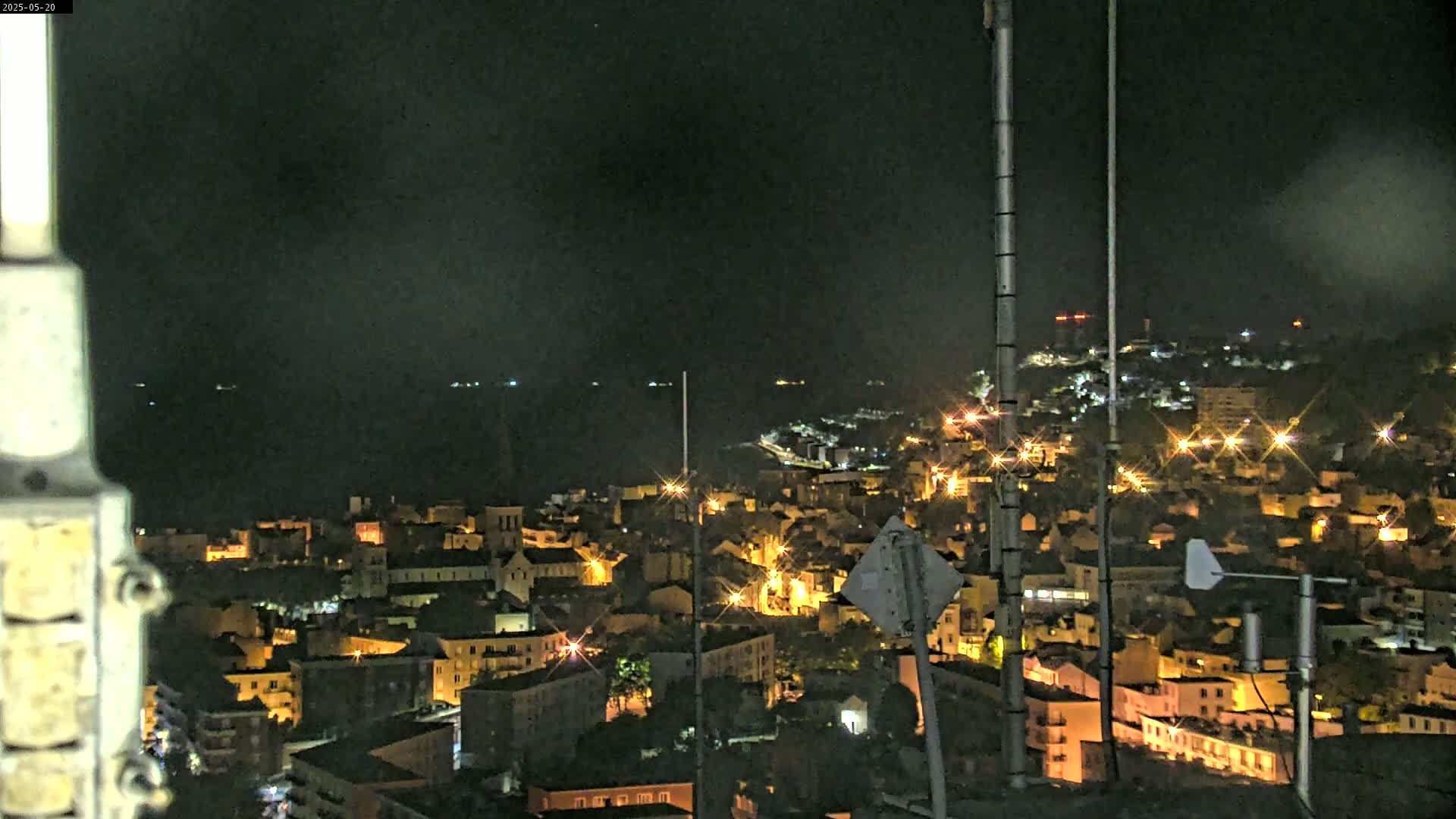 A nighttime view of a coastal town illuminated by streetlights, with a dark body of water visible in the distance under a clear sky.
