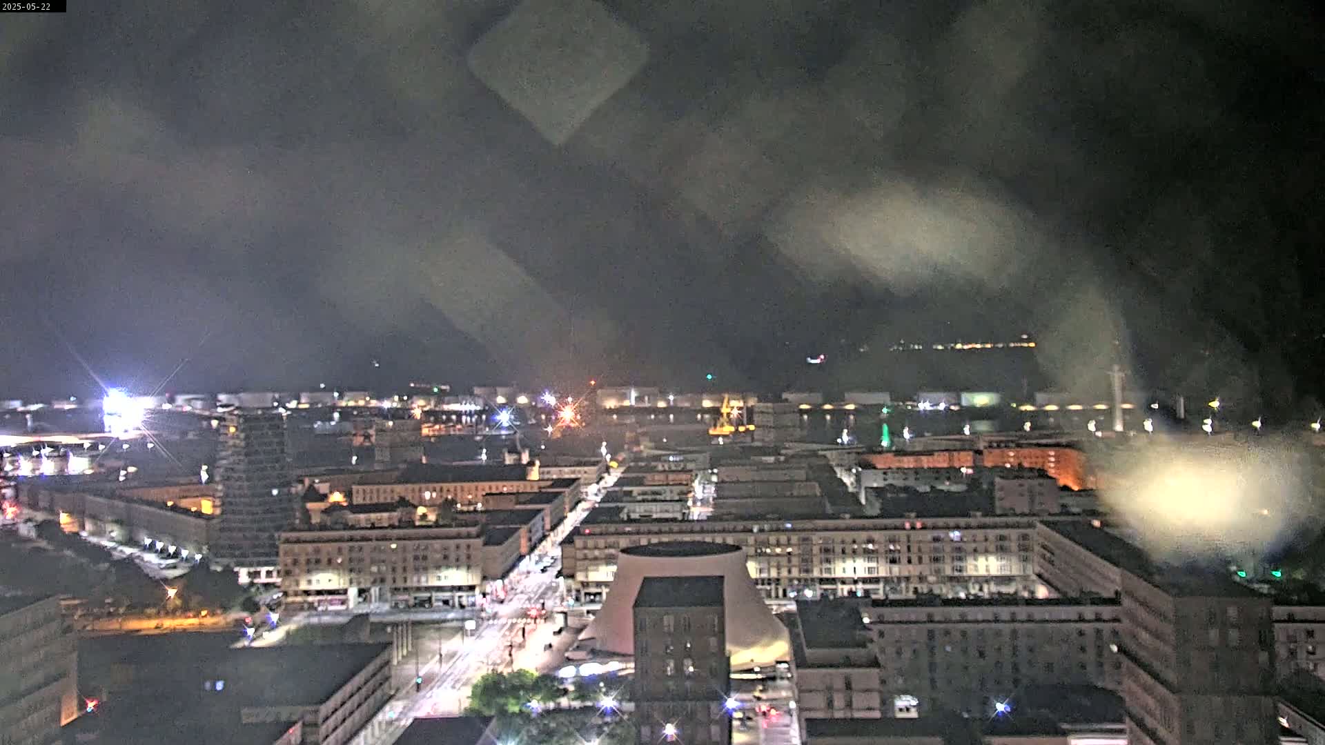 A nighttime, high-angle view of a city illuminated with streetlights and building lights under a cloudy sky.
