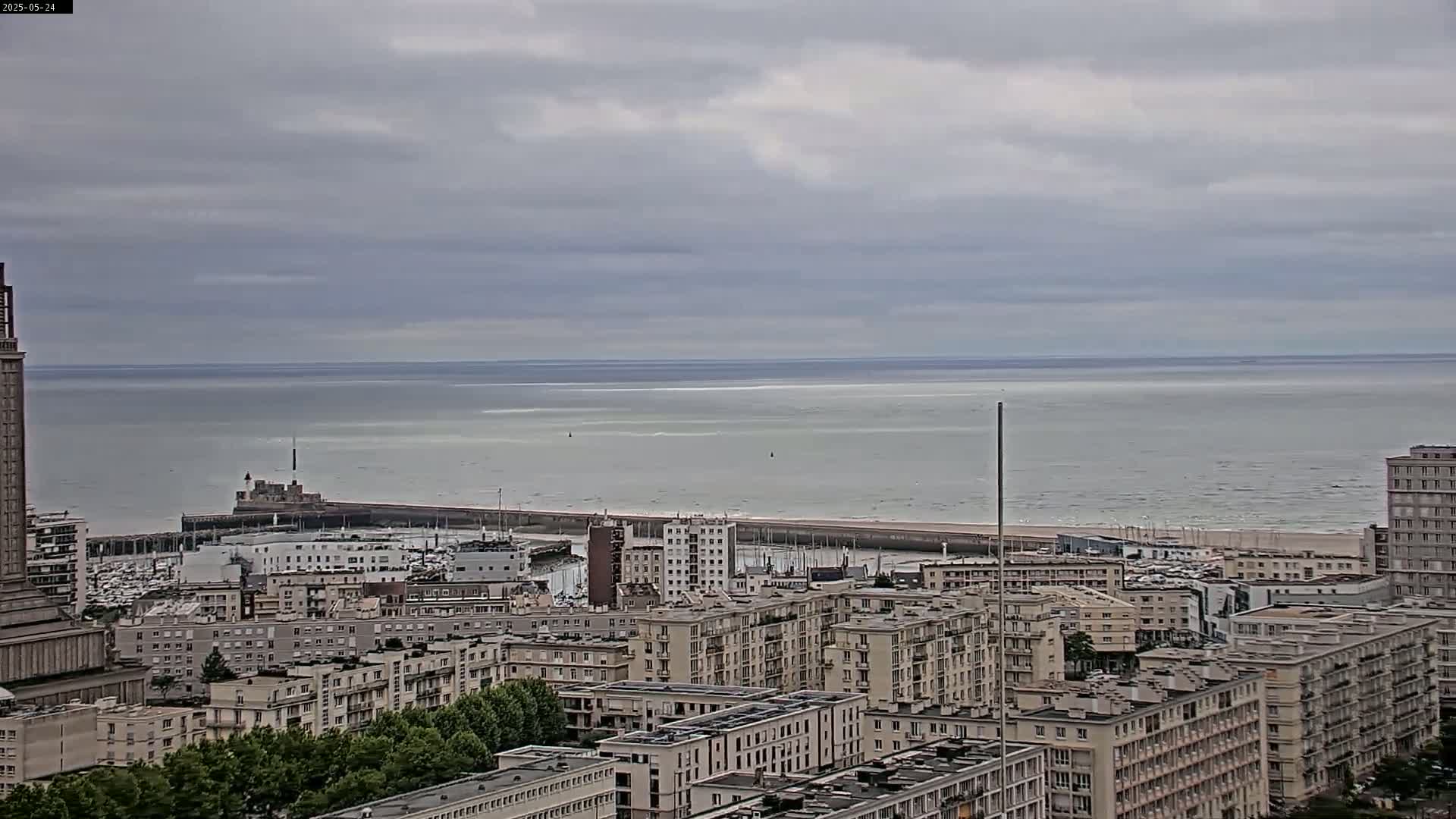 A cityscape of multi-story buildings overlooks a calm sea under a cloudy sky.