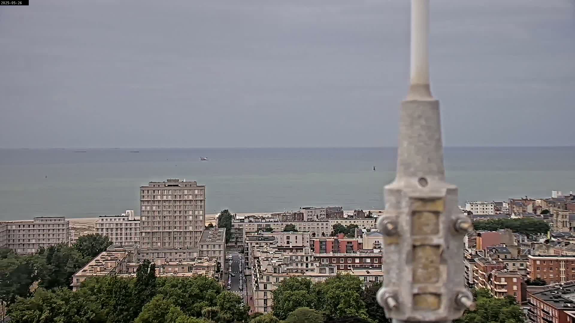 A coastal city scene is visible under an overcast sky, with a body of water in the background and a tall building in the foreground.