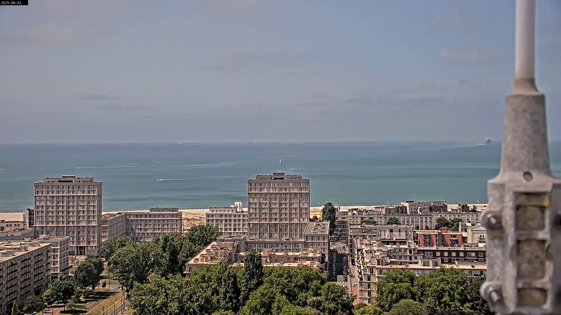 A coastal city with several high-rise buildings is visible, under a mostly clear sky, with a calm ocean in the background.
