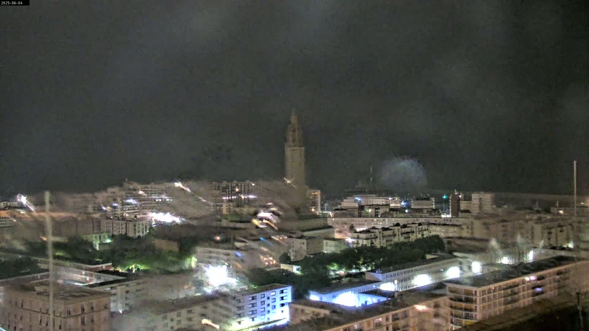 A nighttime view of a city with a tall tower in the distance, under a dark, cloudy sky.