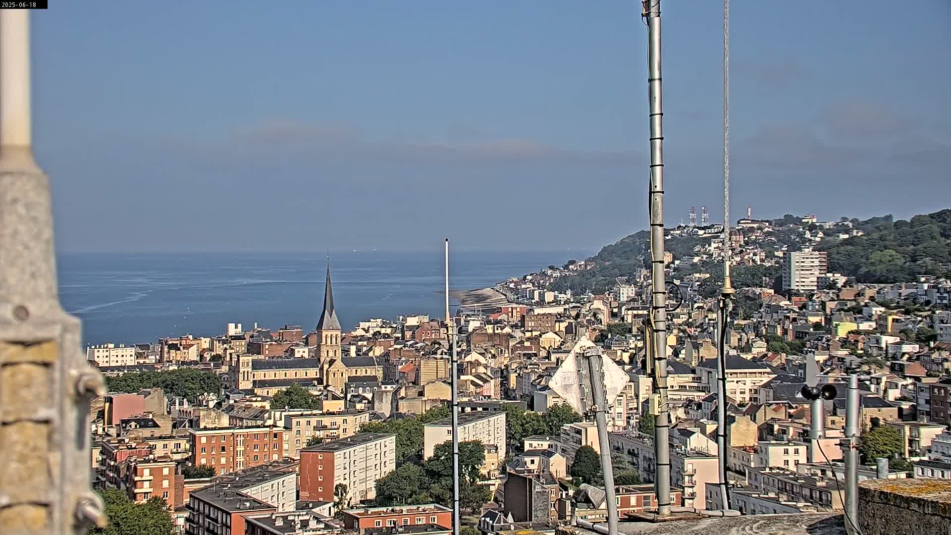A coastal city with numerous buildings and a church steeple is visible, extending to a calm ocean under a clear sky.