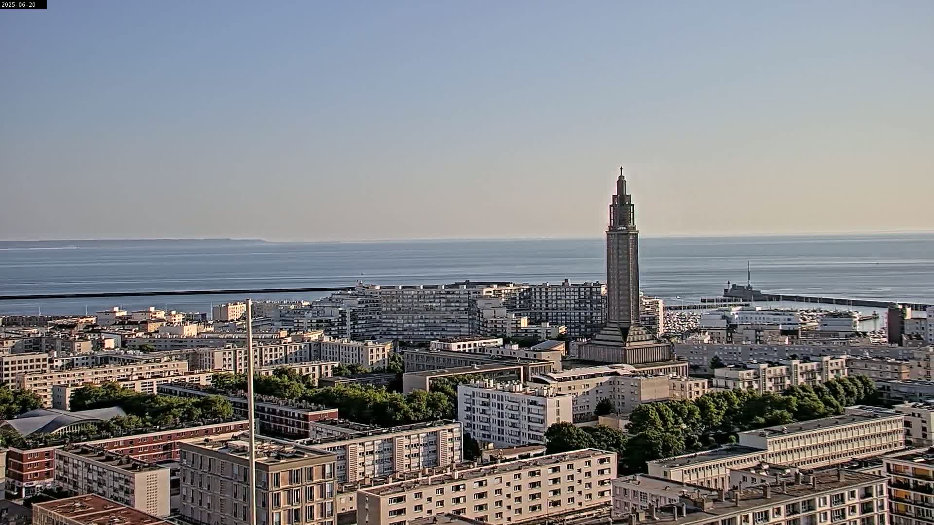 A coastal city with a tall tower is visible, under a clear sky and calm ocean conditions.