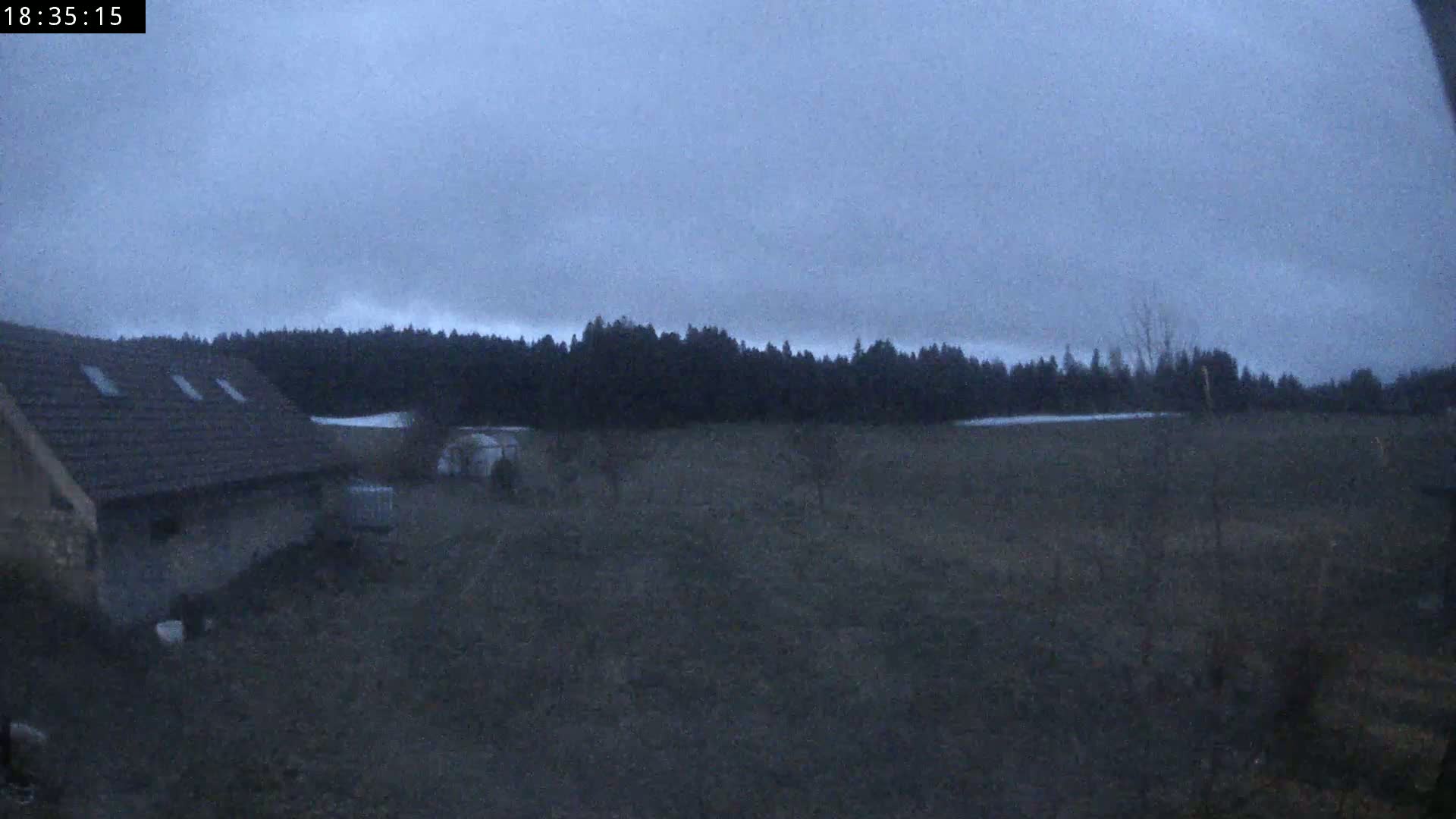 A dark, overcast sky looms over a rural landscape featuring a stone building, a field, and a line of trees in the distance.