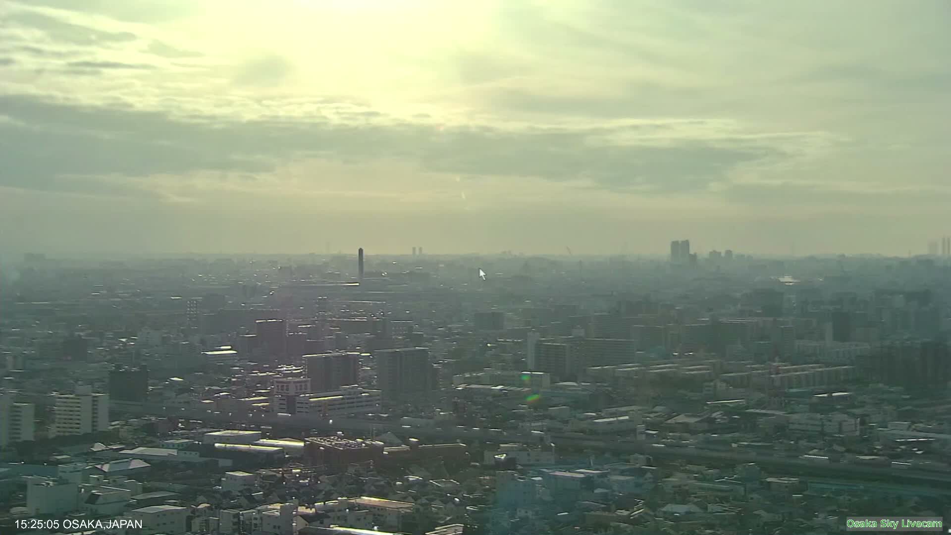 A sprawling urban landscape is visible under a hazy, overcast sky with muted sunlight attempting to break through the clouds.