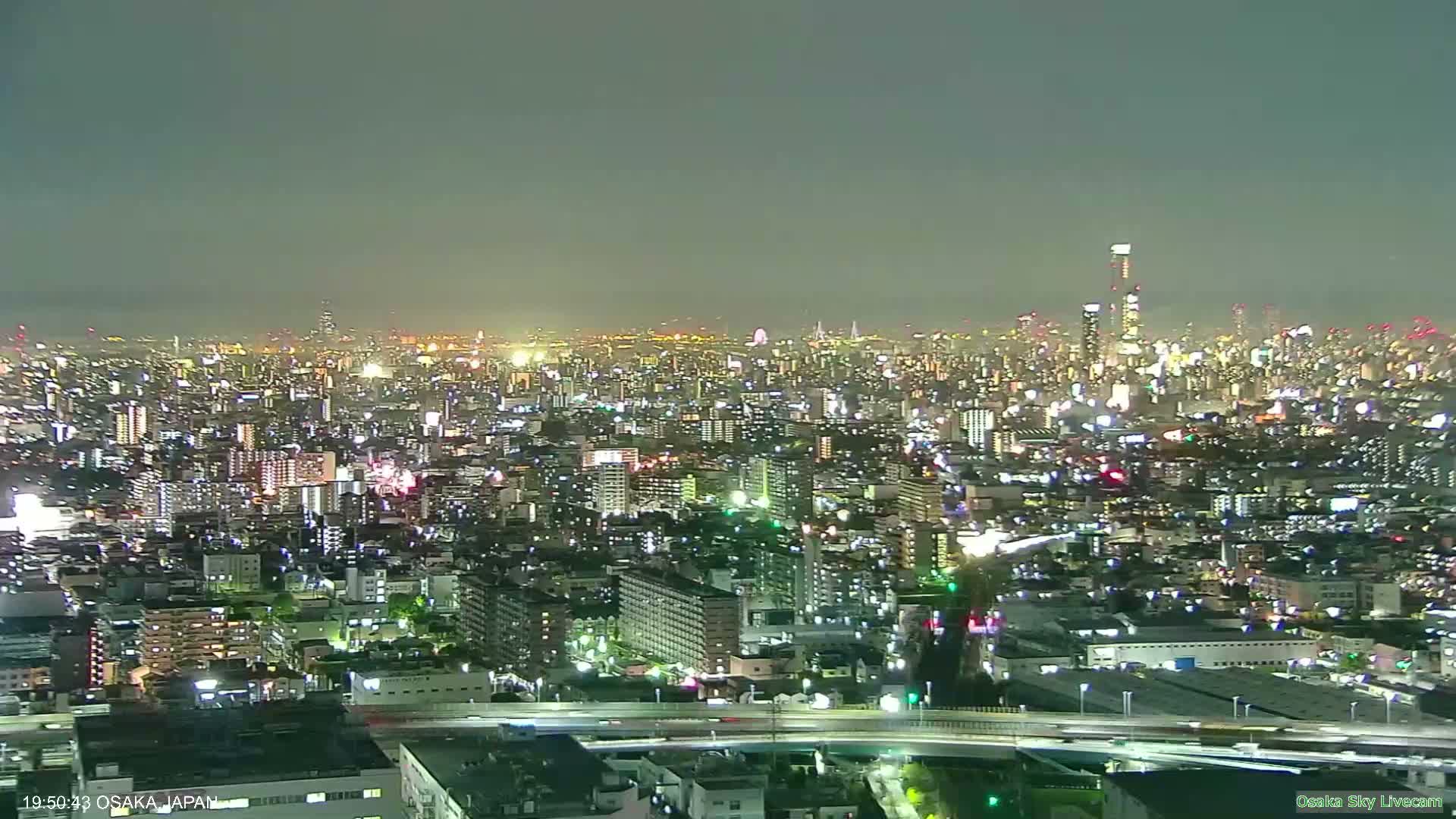 A sprawling urban landscape is visible under a hazy, overcast sky with muted sunlight attempting to break through the clouds.