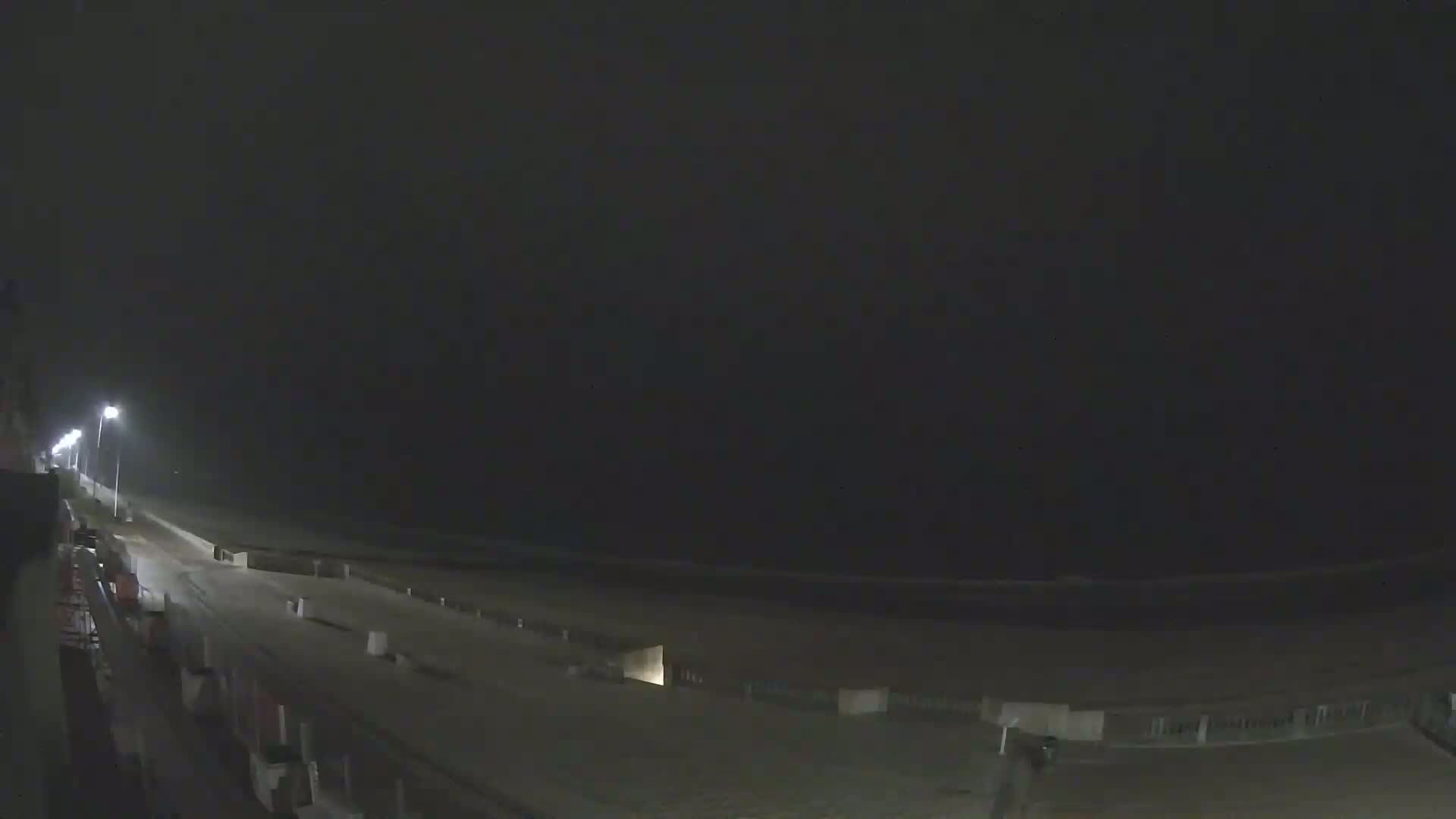 A nighttime view of a dimly lit beach boardwalk and sandy shore under a dark, overcast sky.