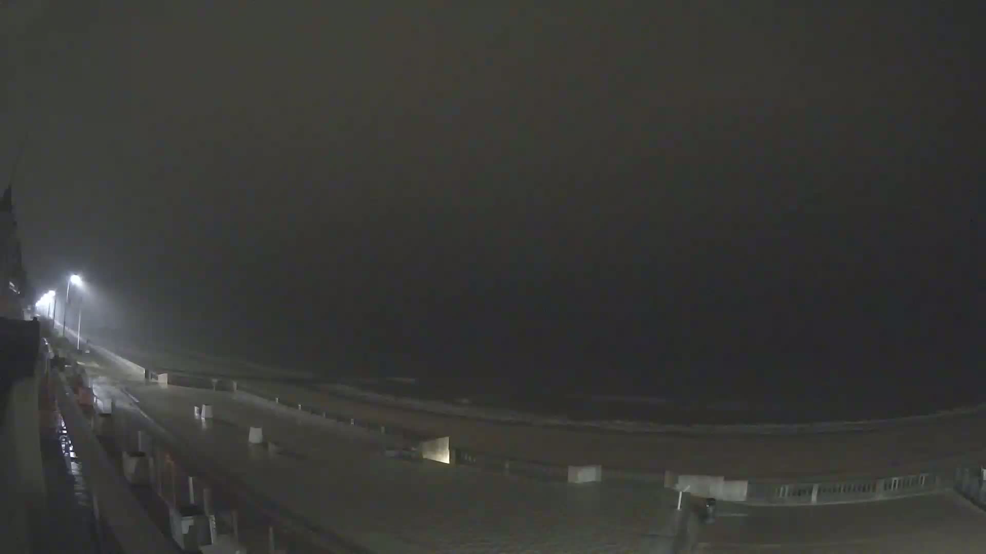 A nighttime view of a rain-soaked beachfront boardwalk under heavy overcast skies.