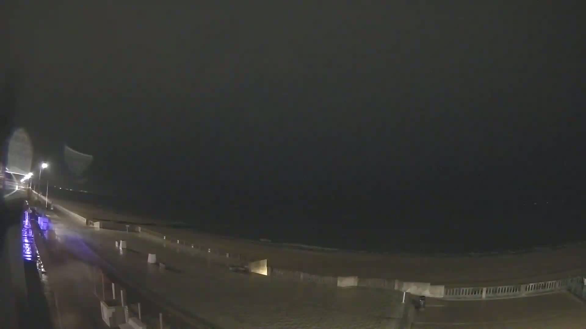 A nighttime view of a wet boardwalk and beach under a dark, overcast sky.