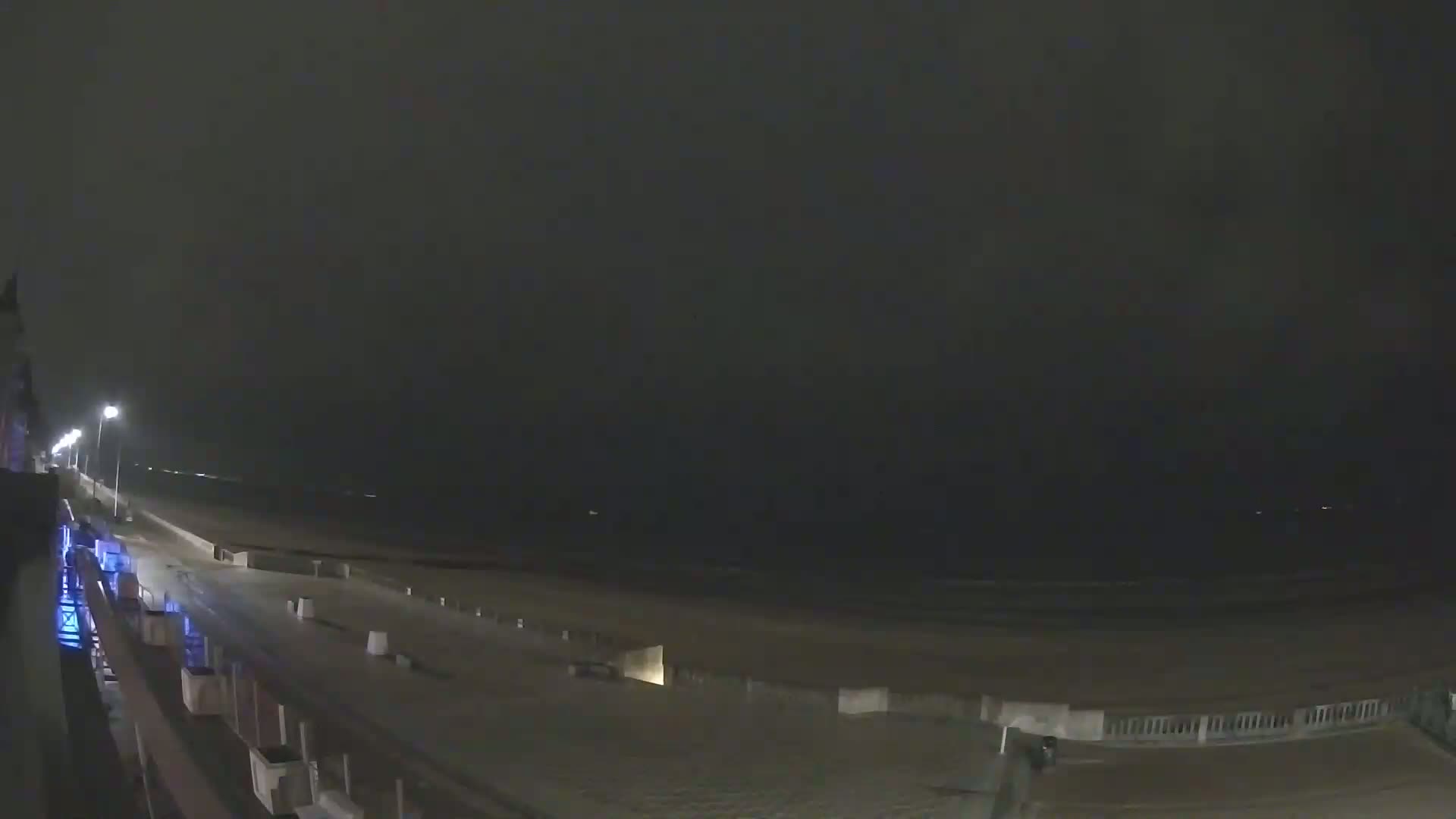 A dark, nighttime beach scene shows a mostly empty boardwalk and beach under an overcast sky.