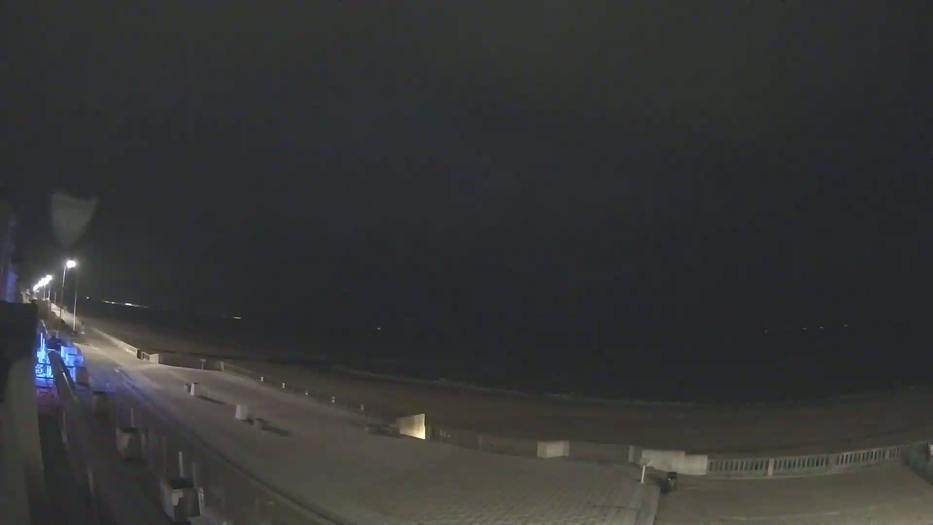 A nighttime view of a dark beach and boardwalk under a mostly clear sky.