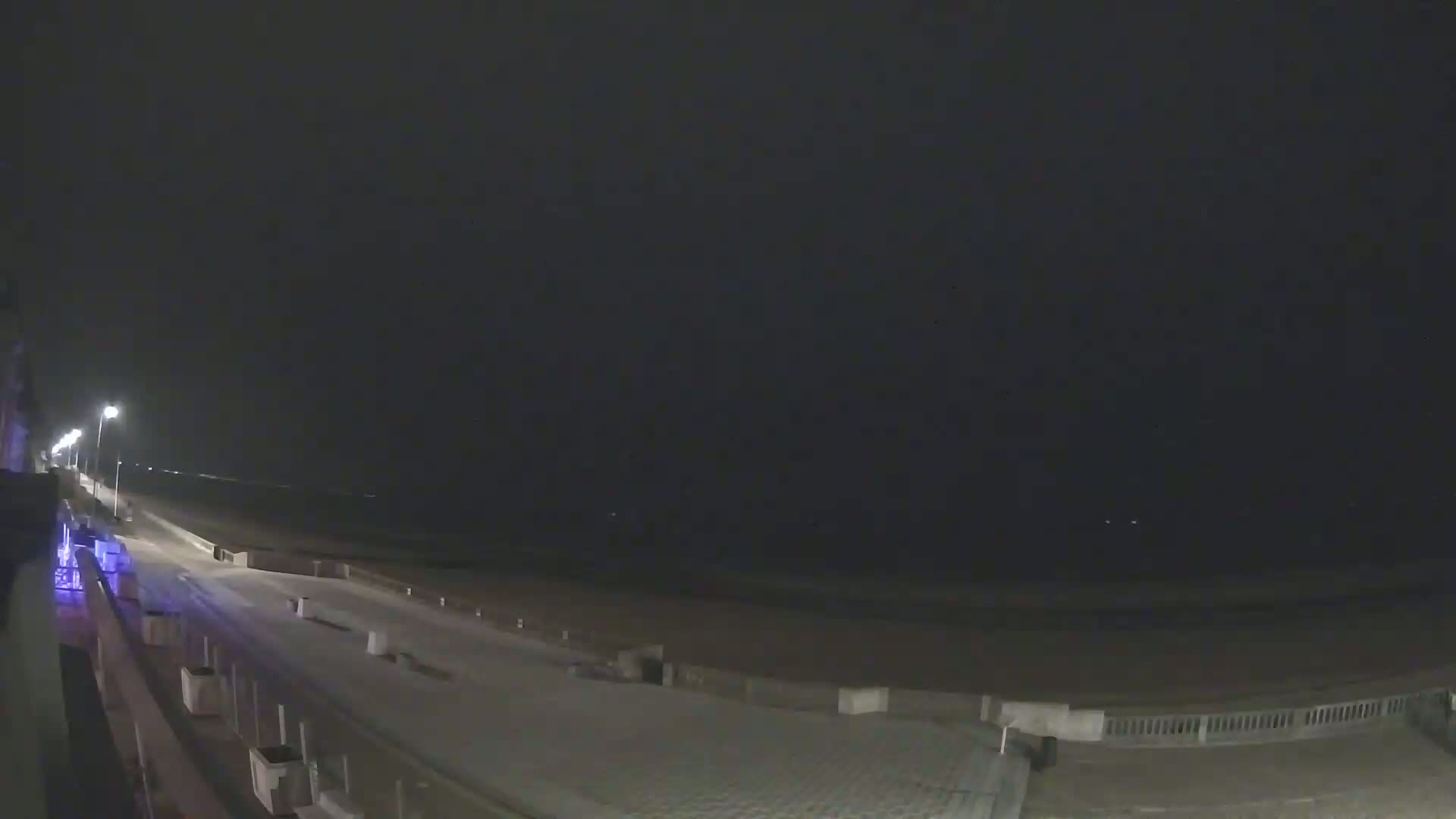 A nighttime view of a snow-covered boardwalk next to a dark beach under a cloudy sky.