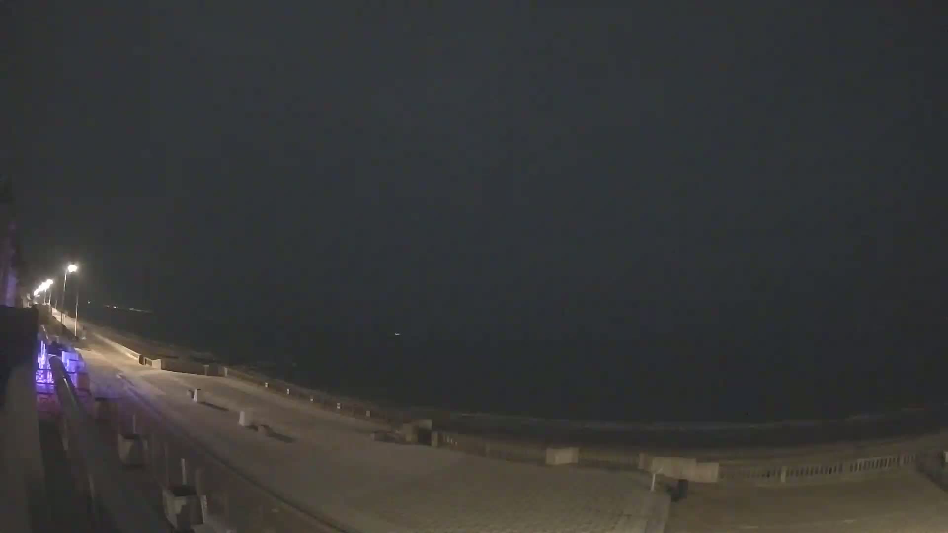 A nighttime view of a snow-covered seaside promenade extending to a dark ocean under a cloudy sky.