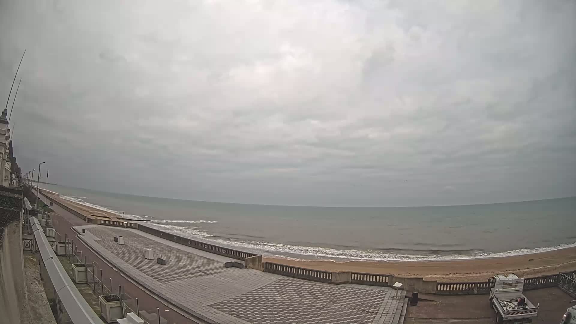A paved seaside promenade overlooks a calm, gray ocean under an overcast sky.