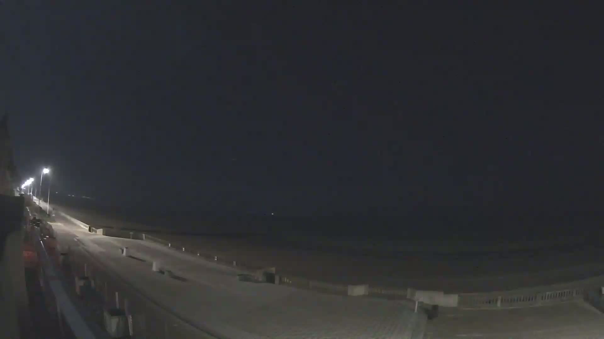A nighttime view of a mostly empty paved beachfront path and beach under a dark, clear sky.