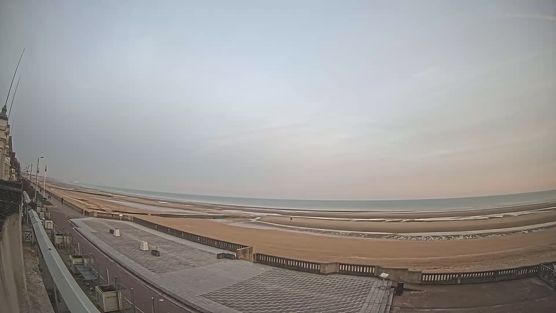A wide, sandy beach stretches to a calm, light-grey sea under an overcast sky.