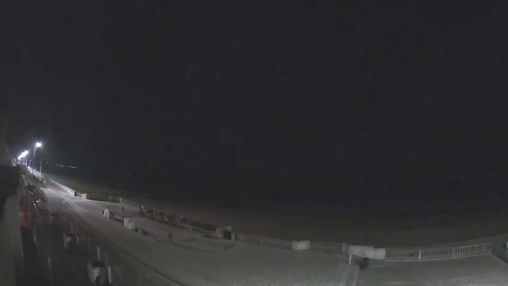 A nighttime view of a mostly empty beach boardwalk and shoreline under a dark sky.