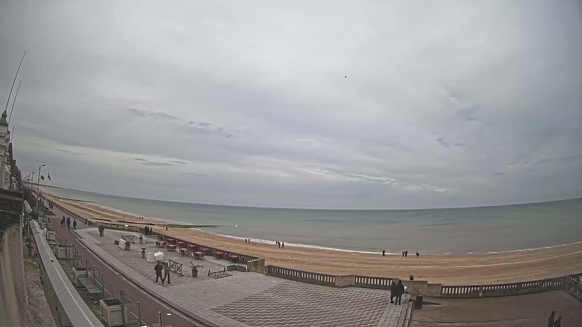 A paved seaside promenade overlooks a wide, sandy beach and calm, gray-green ocean under an overcast sky.