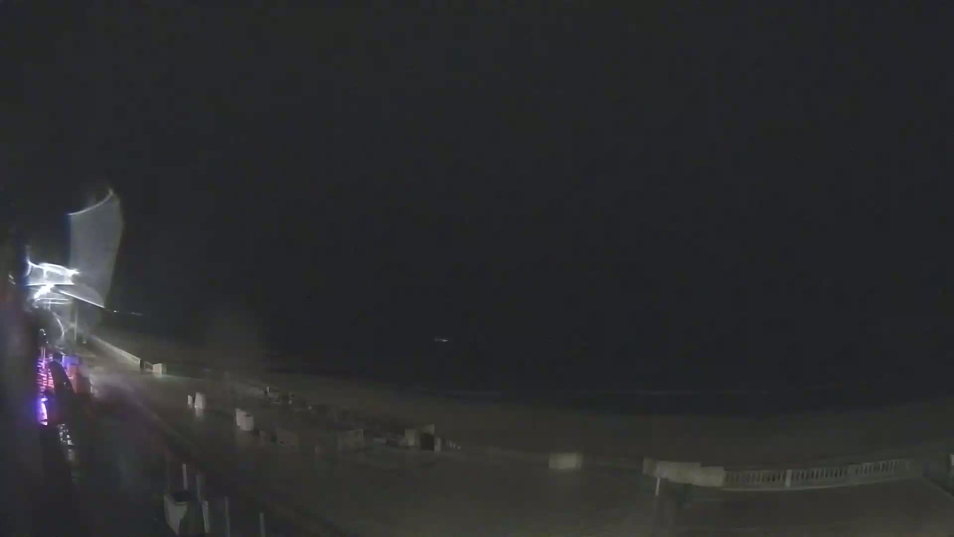 A nighttime, stormy view of a beach with a dark sky and rain-slicked pavement.