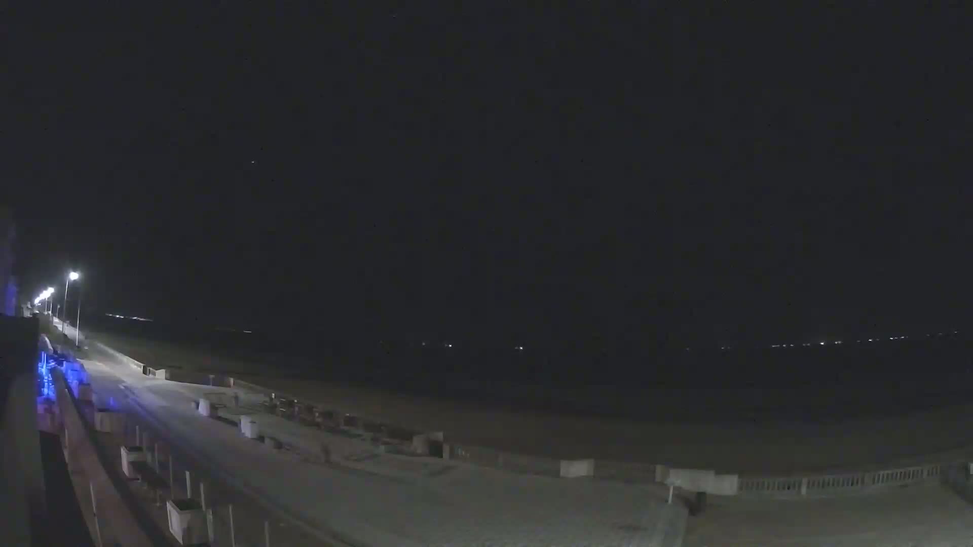 A nighttime view of a beach with a boardwalk and streetlights, under a clear, dark sky.