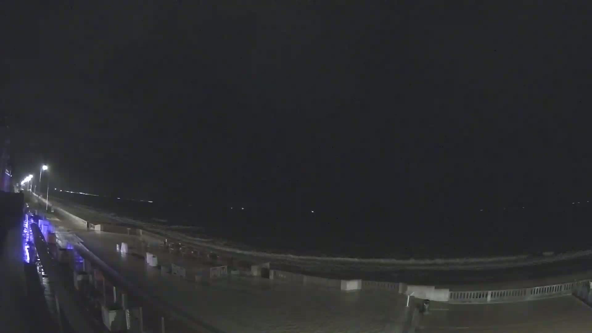 A nighttime view of a dark, wavy ocean next to a dimly lit boardwalk.