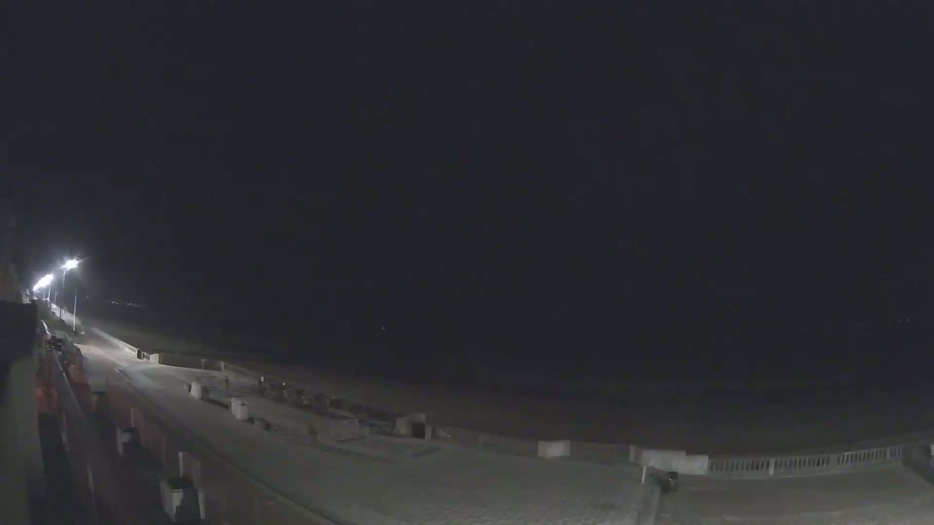 A nighttime view of a beach with a paved walkway and lights, under a dark, clear sky.