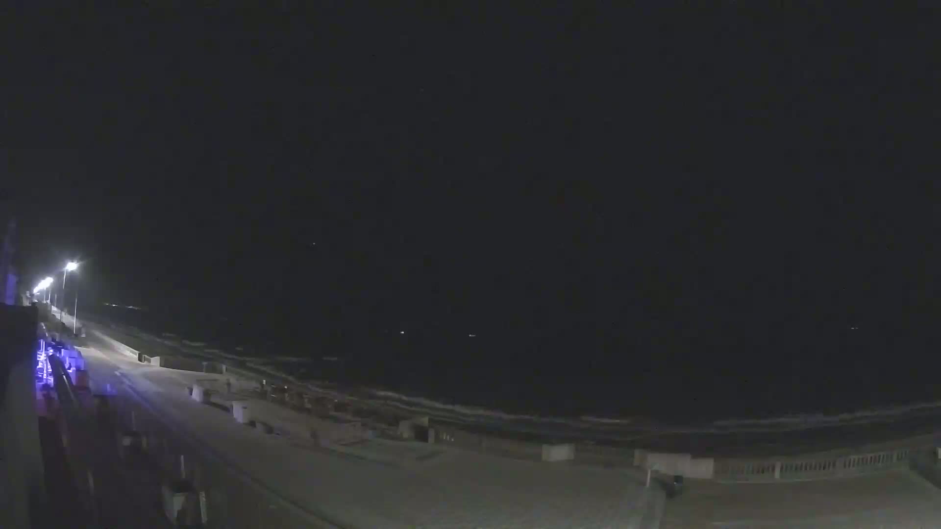 A nighttime view of a mostly empty beach with gently lapping waves under a dark sky.