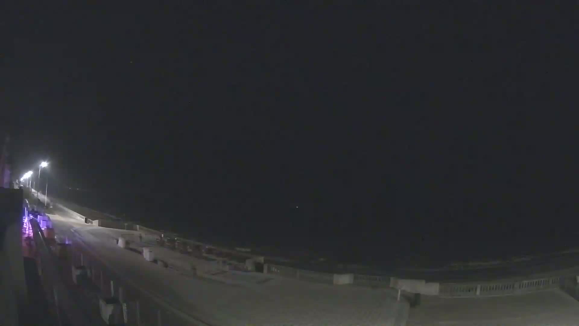 A nighttime view of a dark, seemingly empty beach with a paved walkway and lights along it.