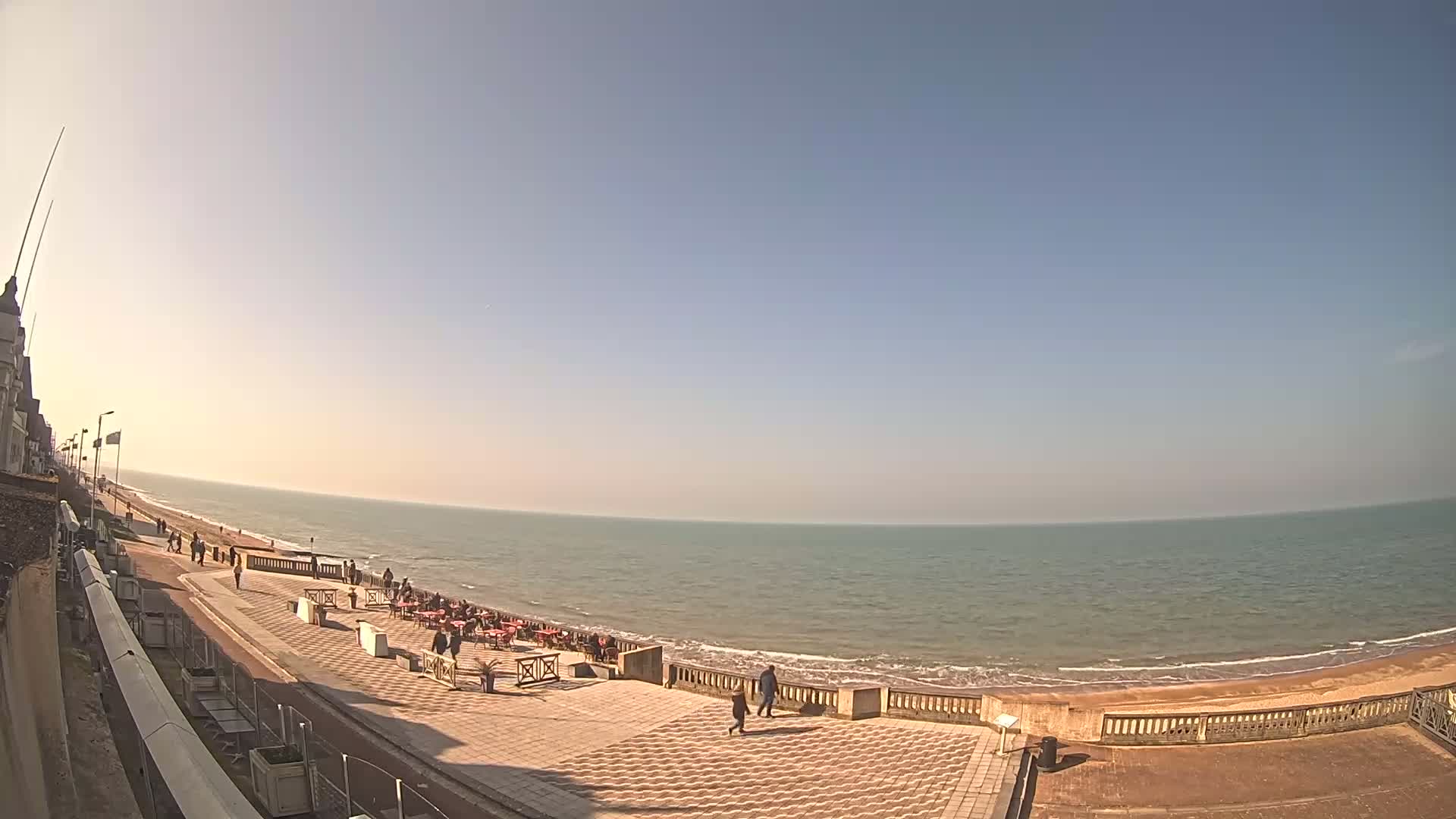A paved seaside promenade overlooks a calm ocean under a clear, sunny sky.